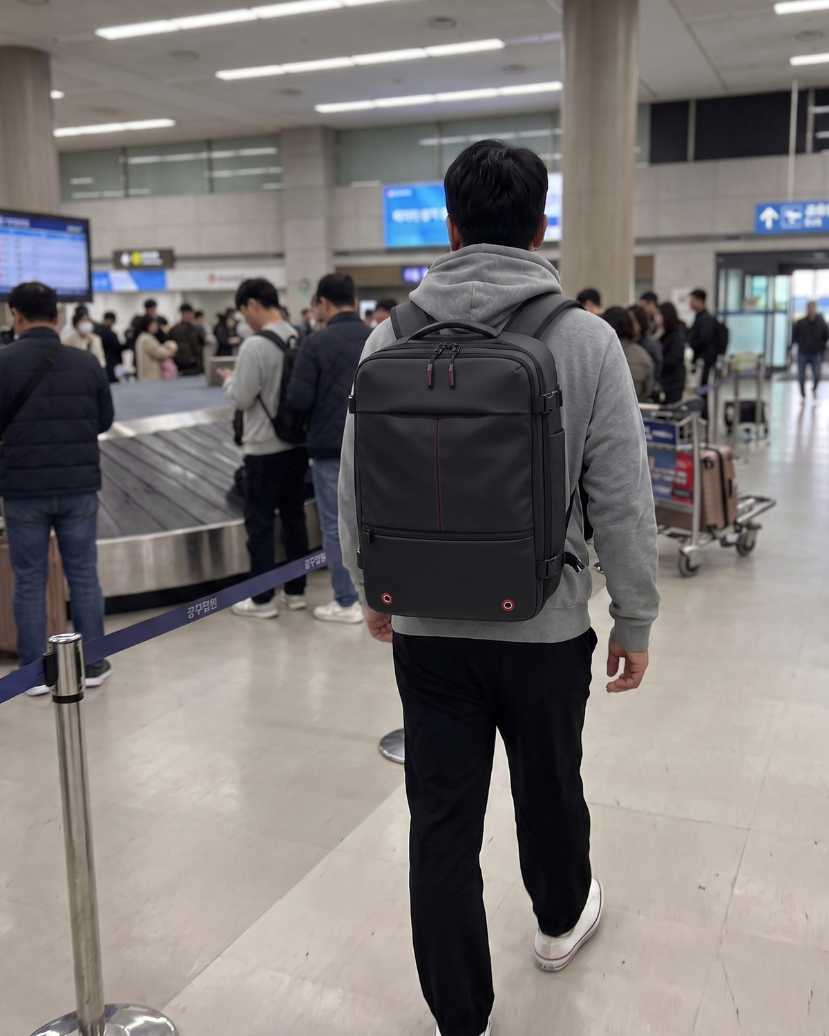수하물 벨트 앞 사람들을 지나 출구로 향하는 VACKS 백팩 여행자